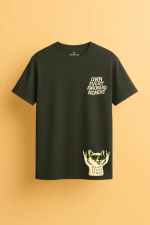 Dark green unisex t-shirt with the phrase “Own Every Awkward Moment” and a cartoon cat wearing sunglasses making rock signs and sticking out its tongue front view